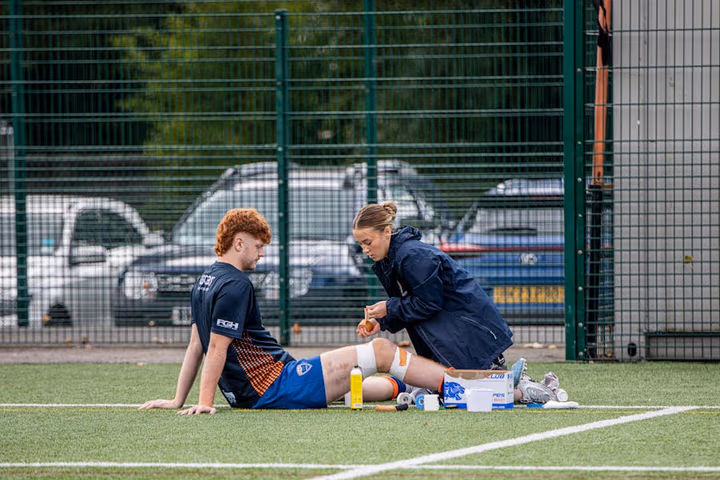 Kinésithérapeute traitant une blessure d'un athlète sur le terrain de football en extérieur.
